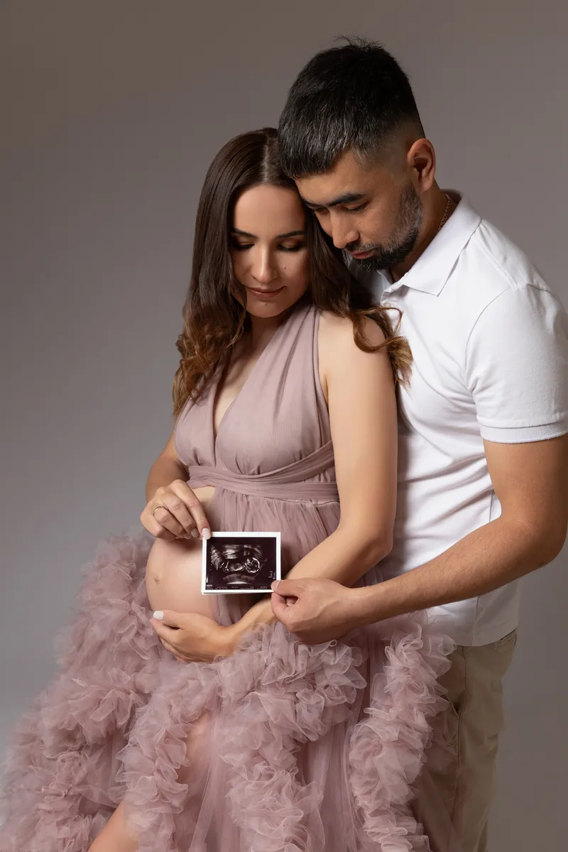 Ein Paar hält ein Ultraschallbild vor einem Babybauch in einem Studio.